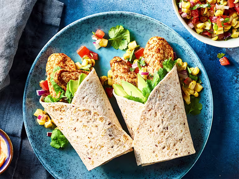 Quorn Tikka Style Mini Fillets and corn salsa in a wrap served on a blue dish with corn salsa on the side.