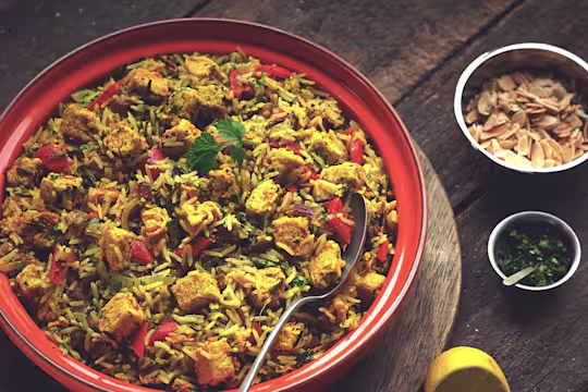 A serving bowl full with hyderabadi chicken biryani made with Quorn pieces, onion, pepper, dates and spices.