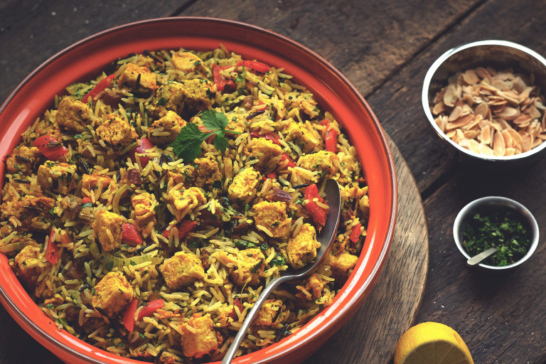 A serving bowl full with hyderabadi chicken biryani made with Quorn pieces, onion, pepper, dates and spices.