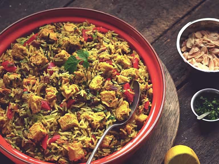 A serving bowl full with hyderabadi chicken biryani made with Quorn pieces, onion, pepper, dates and spices.