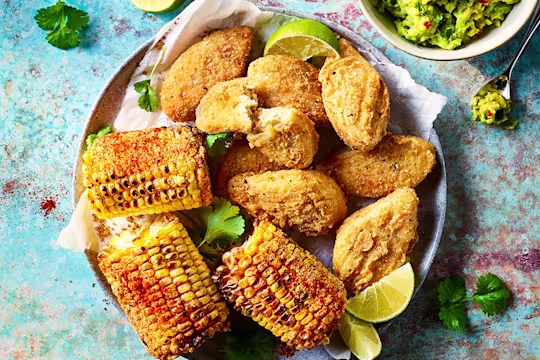 "Quorn Southern Fried wings served alongside corn on the cob with a bowl of guacamole in a bowl on the side.