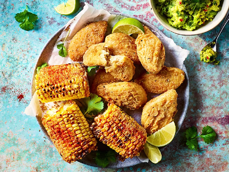"Quorn Southern Fried wings served alongside corn on the cob with a bowl of guacamole in a bowl on the side.
