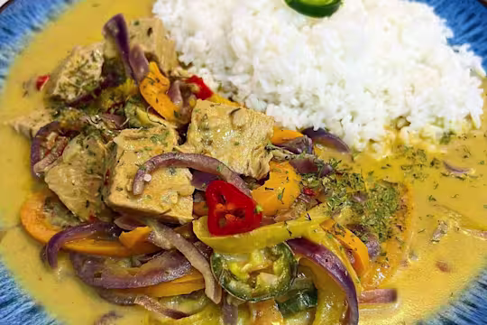 Thai inspired Quorn Beef Roast Curry with a side of rice in a blue bowl garnished with chilli.
