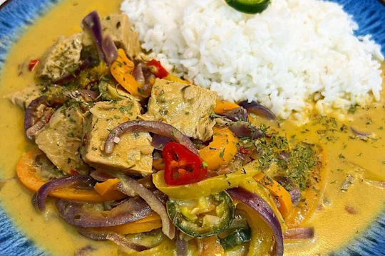 Thai inspired Quorn Beef Roast Curry with a side of rice in a blue bowl garnished with chilli.