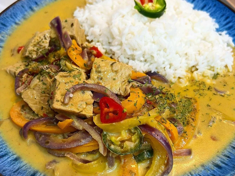 Thai inspired Quorn Beef Roast Curry with a side of rice in a blue bowl garnished with chilli.