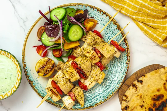 A ceramic plate with Quorn Vegetarian Fillets and halloumi on skewers with red bell pepper plus a side salad.