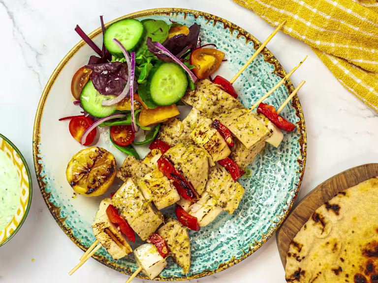 A ceramic plate with Quorn Vegetarian Fillets and halloumi on skewers with red bell pepper plus a side salad.