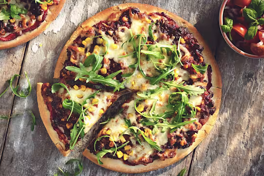 A pizza topped with cheese, arugula, corn, and Quorn Meatless Grounds.