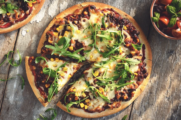 A pizza topped with cheese, arugula, corn, and Quorn Meatless Grounds.