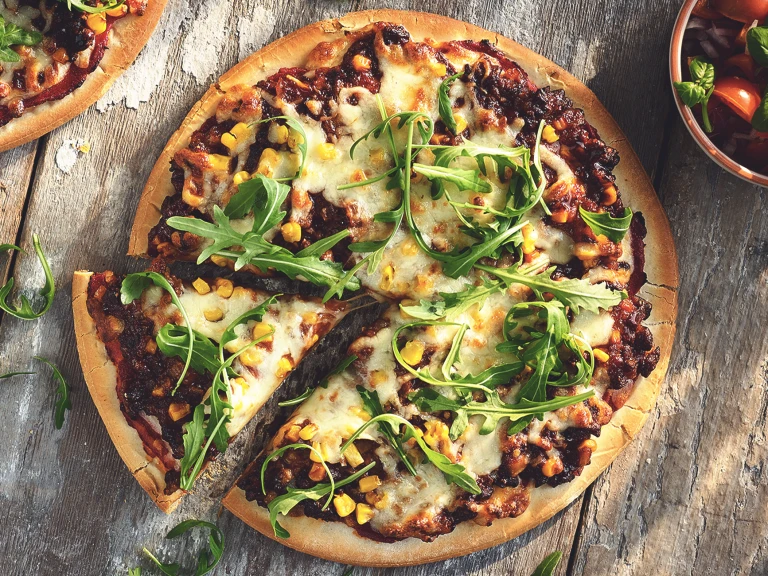 A pizza topped with cheese, arugula, corn, and Quorn Meatless Grounds.