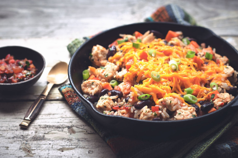 Rice, kidney beans, and Quorn Pieces in a cast iron skillet topped with cheese and green onions with a small dish of salsa on the side.