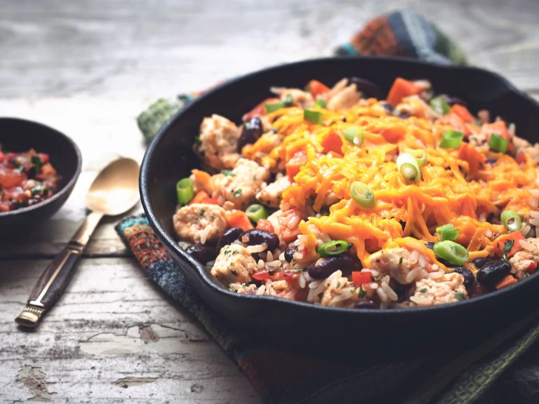 Rice, kidney beans, and Quorn Pieces in a cast iron skillet topped with cheese and green onions with a small dish of salsa on the side.