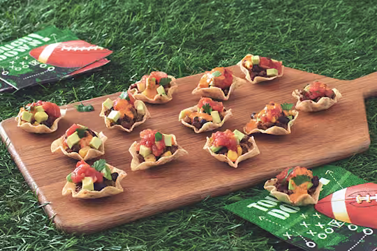 Mini Tortilla Chip Bowls Filled with Quorn Grounds, black beans, salsa, queso, avocado, and cilantro arranged on a board with game day napkins placed around it.
