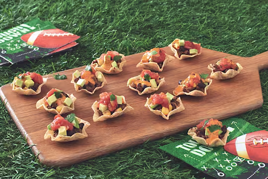 Mini Tortilla Chip Bowls Filled with Quorn Grounds, black beans, salsa, queso, avocado, and cilantro arranged on a board with game day napkins placed around it.