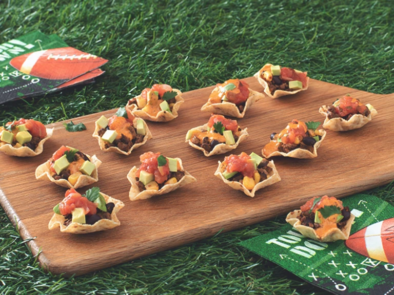 Mini Tortilla Chip Bowls Filled with Quorn Grounds, black beans, salsa, queso, avocado, and cilantro arranged on a board with game day napkins placed around it.