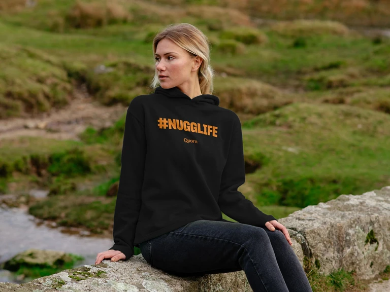 A woman sat in a country-side setting wearing a black #nugglife hoodie.