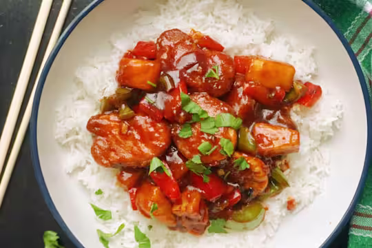 Vegetarian Sweet And Sour with Quorn Crispy Nuggets served on a bed of rice with chopsticks on the side.