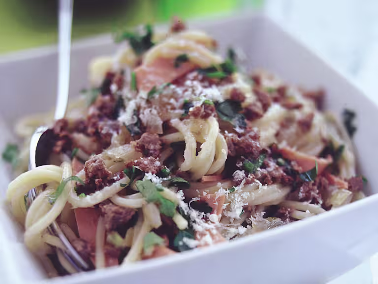 Close up shot of Quorn Mince and spaghetti in a square white bowl garnished with parsley and parmesan cheese.
