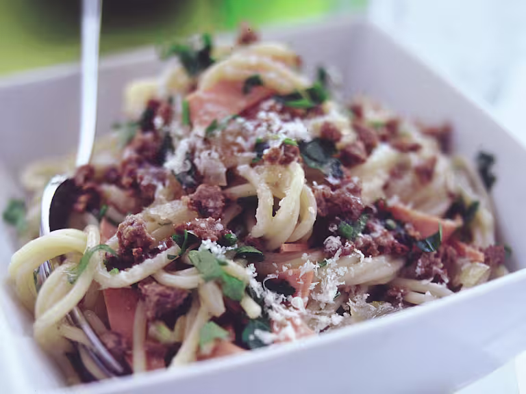 Close up shot of Quorn Mince and spaghetti in a square white bowl garnished with parsley and parmesan cheese.