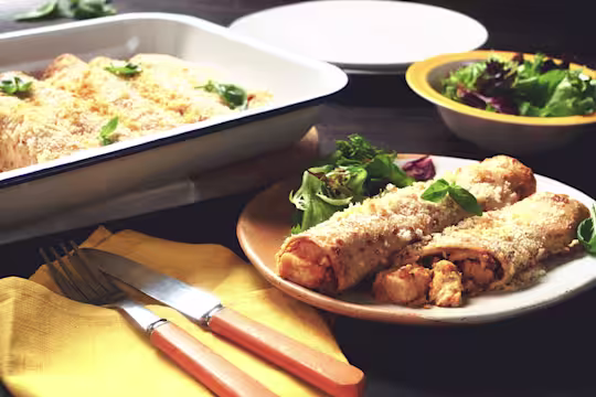 Two baked pancakes filled with Quorn Pieces and vegetables topped with breadcrumbs and cheese plated with a side salad and the full baking dish in the background.