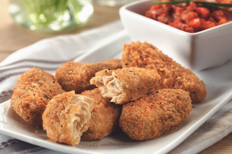 Quorn Southern Fried Bites on a white plate with a dish of red pepper relish in the background.