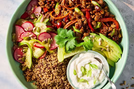 5 spiced Quorn Mince with sliced onions, red pepper, carrots, garlic, radishes, cucumber, seeds and avocado in a blue bowl, with a smaller bowl of cottage cheese, on a white background.