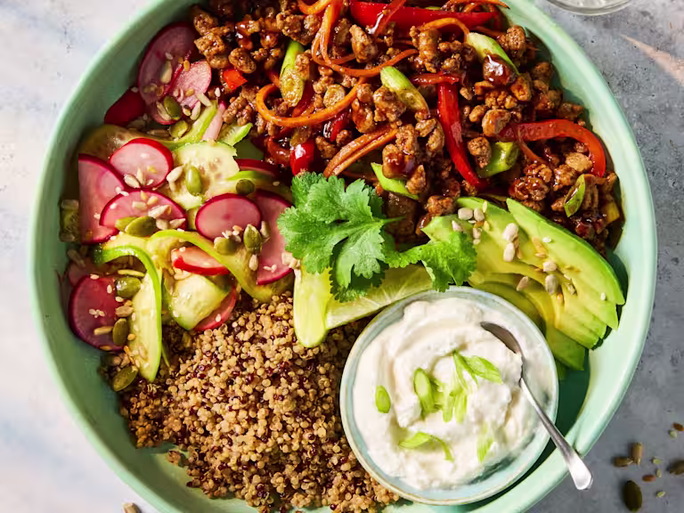 5 spiced Quorn Mince with sliced onions, red pepper, carrots, garlic, radishes, cucumber, seeds and avocado in a blue bowl, with a smaller bowl of cottage cheese, on a white background.