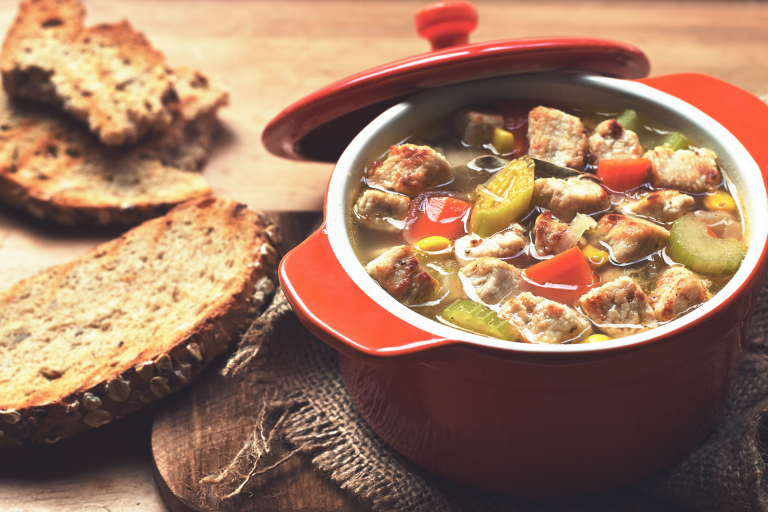 A vegetable soup with carrots, celery, sweetcorn, and Quorn Pieces in a red Dutch oven with toasted wholegrain bread on the side.