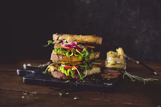 A vegan club sandwich made with Quorn Vegan Pepperoni Slices, pickled onions, white bean spread, tomatoes, and pea shoots.