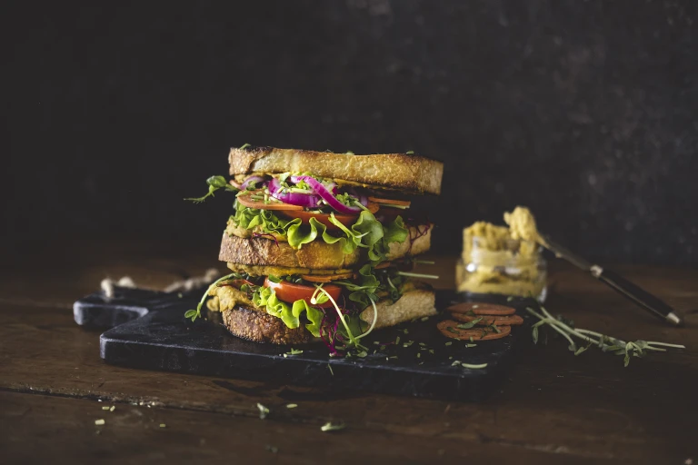 A vegan club sandwich made with Quorn Vegan Pepperoni Slices, pickled onions, white bean spread, tomatoes, and pea shoots.