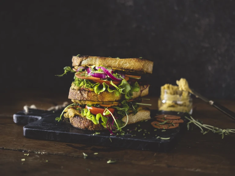 A vegan club sandwich made with Quorn Vegan Pepperoni Slices, pickled onions, white bean spread, tomatoes, and pea shoots.