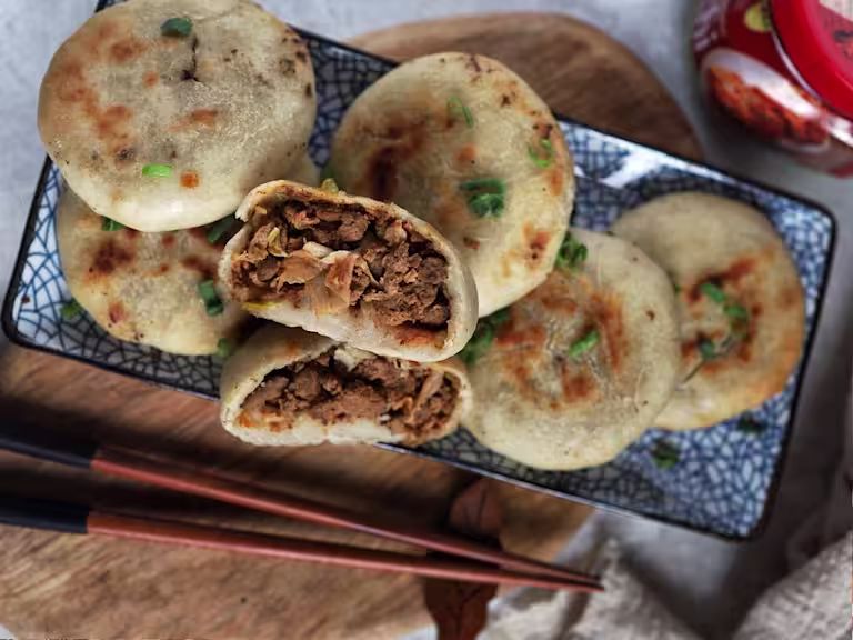 Six vegetarian air fryer kimchi buns arranged on a plate with one halved to reveal a filling of Quorn Mince and kimchi.