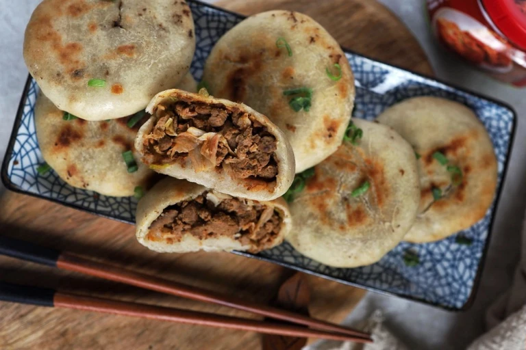 Six vegetarian air fryer kimchi buns arranged on a plate with one halved to reveal a filling of Quorn Mince and kimchi.