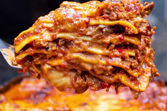 Piece of Quorn Lasagne on a spatula in front of a tray of lasagne