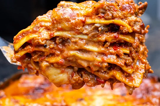Piece of Quorn Lasagne on a spatula in front of a tray of lasagne