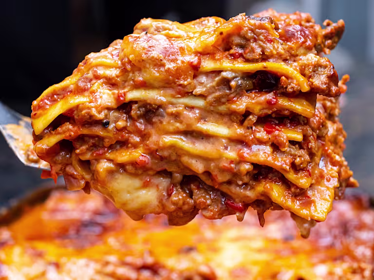 Piece of Quorn Lasagne on a spatula in front of a tray of lasagne