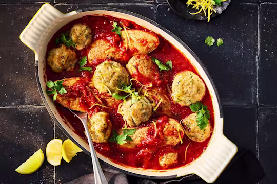 Arabiatta stew with parmesan dumplings and Quorn fillets in a white serving dish on a black background.