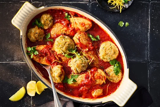 Arabiatta stew with parmesan dumplings and Quorn fillets in a white serving dish on a black background.