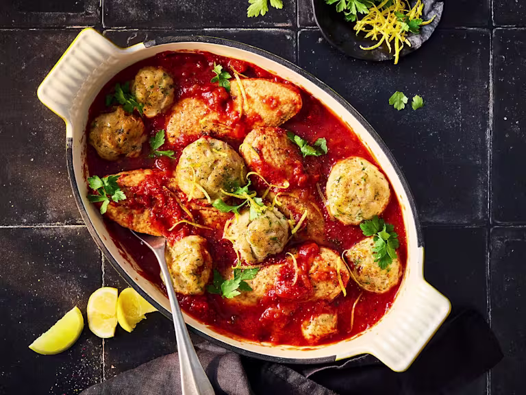 Arabiatta stew with parmesan dumplings and Quorn fillets in a white serving dish on a black background.
