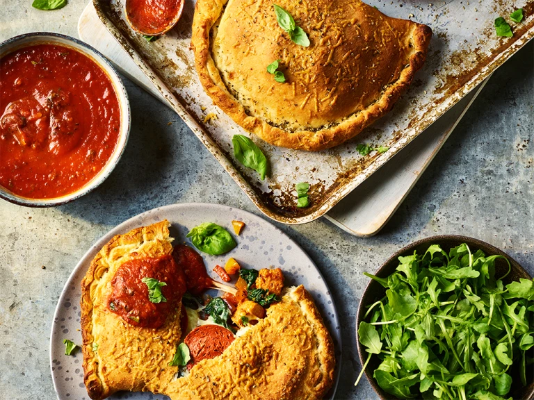 Two Quorn Vegetarian Calzones, one split to display the filling with sauce and greens on the side.