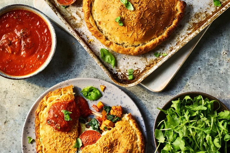 Two Quorn Vegetarian Calzones, one split to display the filling with sauce and greens on the side.