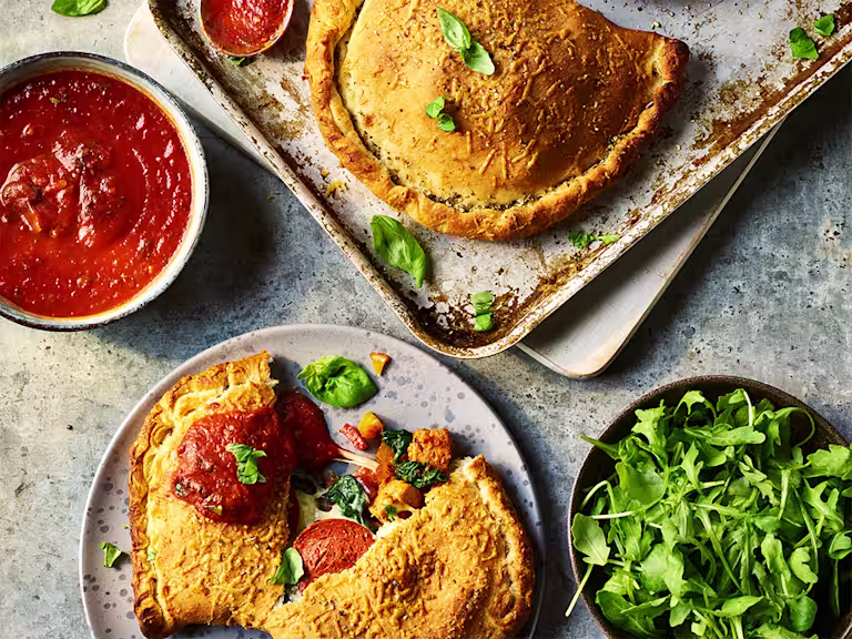 Two Quorn Vegetarian Calzones, one split to display the filling with sauce and greens on the side.