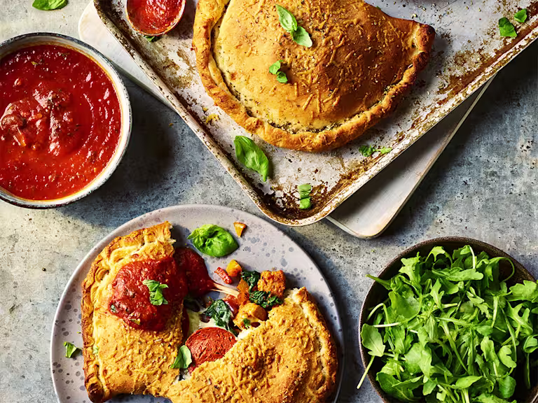 Two Quorn Vegetarian Calzones, one split to display the filling with sauce and greens on the side.