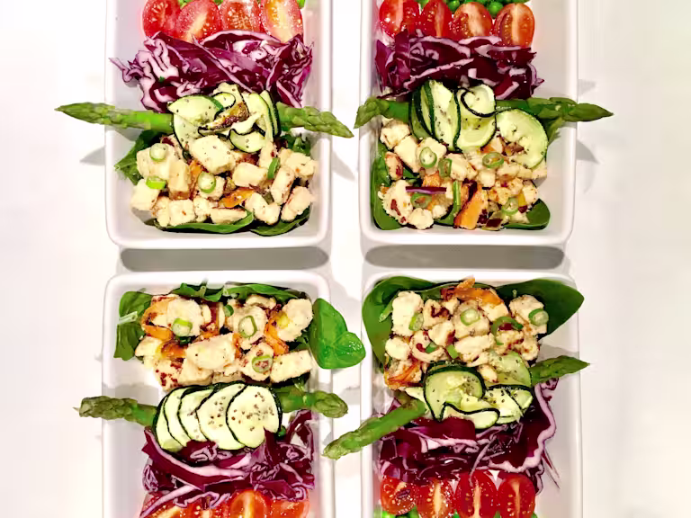 Meal prep idea of Quorn Pieces on top of asparagus, spinach, courgette and red cabbage, topped with chopped spring onion