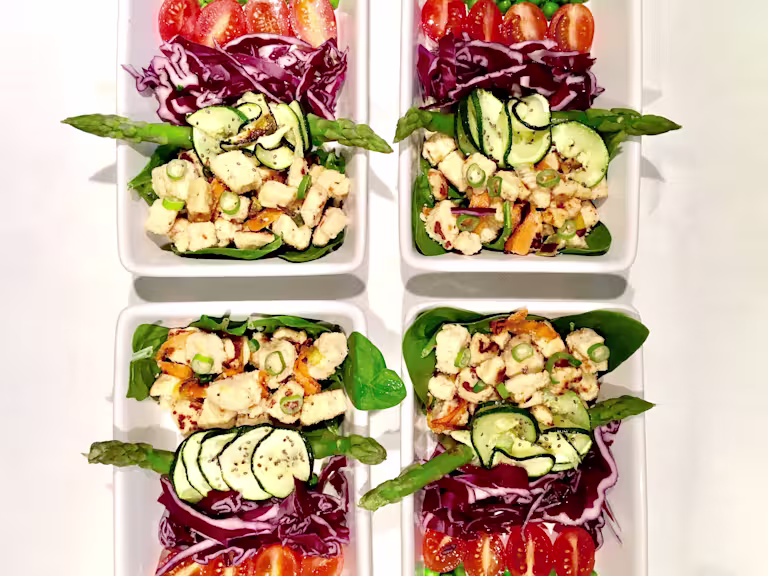 Meal prep idea of Quorn Pieces on top of asparagus, spinach, courgette and red cabbage, topped with chopped spring onion