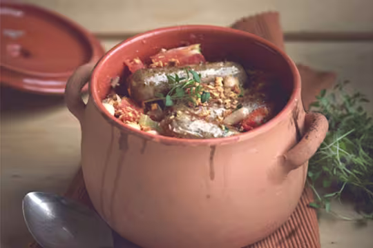 A clay pot filled with a cassoulet made with Quorn Sausages, tomatoes, and white beans.