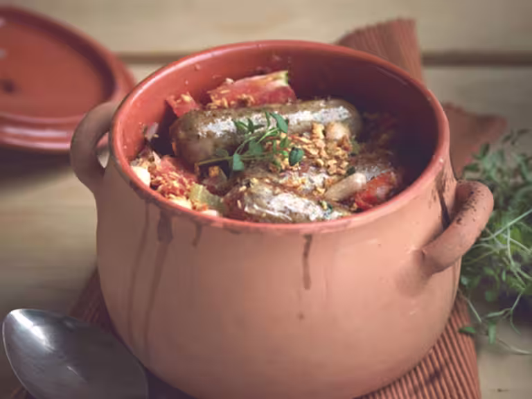A clay pot filled with a cassoulet made with Quorn Sausages, tomatoes, and white beans.