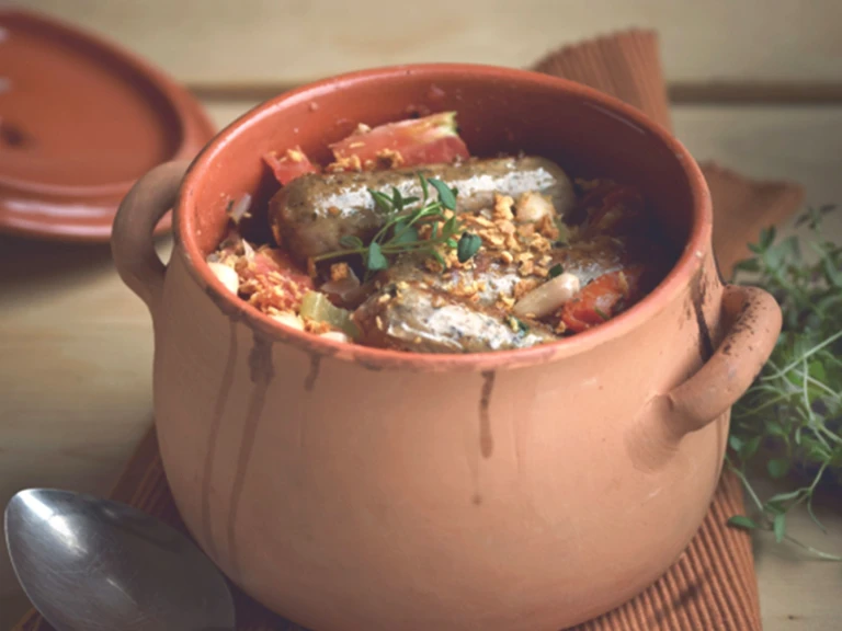 A clay pot filled with a cassoulet made with Quorn Sausages, tomatoes, and white beans.