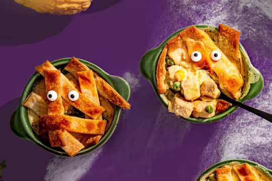 Two mini vegetarian chicken pies with candy eyes served in green pots one with a spoon poking out.