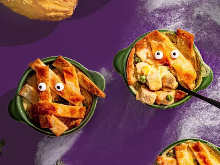 Two mini vegetarian chicken pies with candy eyes served in green pots one with a spoon poking out.